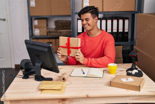 Young hispanic man ecommerce business worker having video call holding package at office