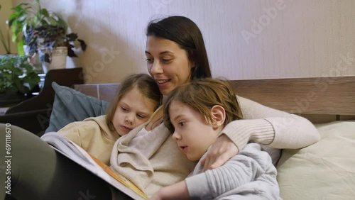 Mom is lying on the bed with her children, reading a bedtime story. Her son and daughter are happily listening to the stories