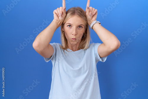 Young caucasian woman wearing casual blue t shirt doing funny gesture with finger over head as bull horns photo