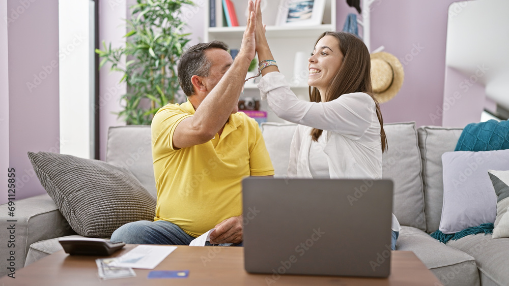Obraz premium Family business win! smiling father and daughter sitting on sofa, high-fiving over home accounting achievement