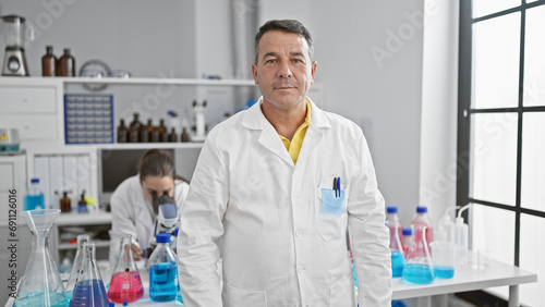 Fototapeta Naklejka Na Ścianę i Meble -  Two confident hispanic scientists, man and woman, together at the lab - smiling faces despite serious research work