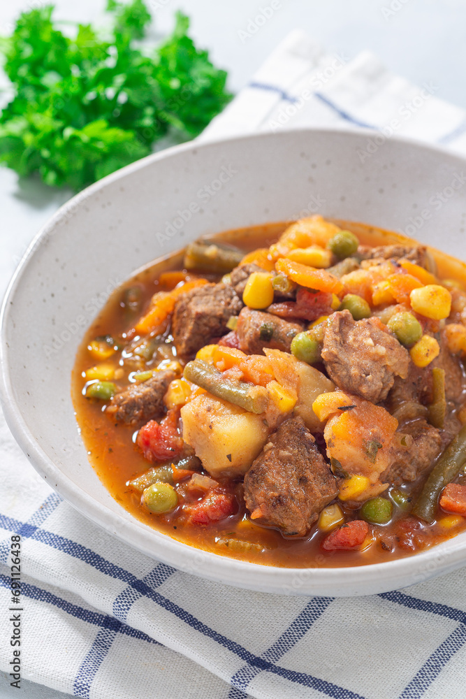 Beef stew with potato, green beans, carrot, peas and corn, in gray bowl, vertical Beef stew with potato, green beans, carrot, peas and corn, in gray bowl, vertical