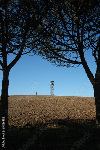 A lookout tower in the Blue Sky Hills of Portugal, framed between two trees on a blue sky day.