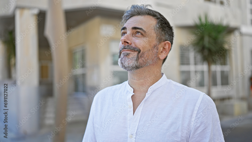 Confident young hispanic man with grey-haired, beaming and looking up at the sky, standing on the sunny city street with urban backdrop, emitting joy and a positive vibe. Confident young hispanic man with grey-haired, beaming and looking up at the sky, standing on the sunny city street with urban backdrop, emitting joy and a positive vibe.