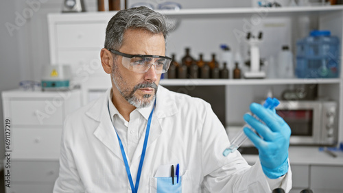 Attractive young hispanic man, grey-haired chemist, concentrating on measuring liquid in test tube at indoor science lab.