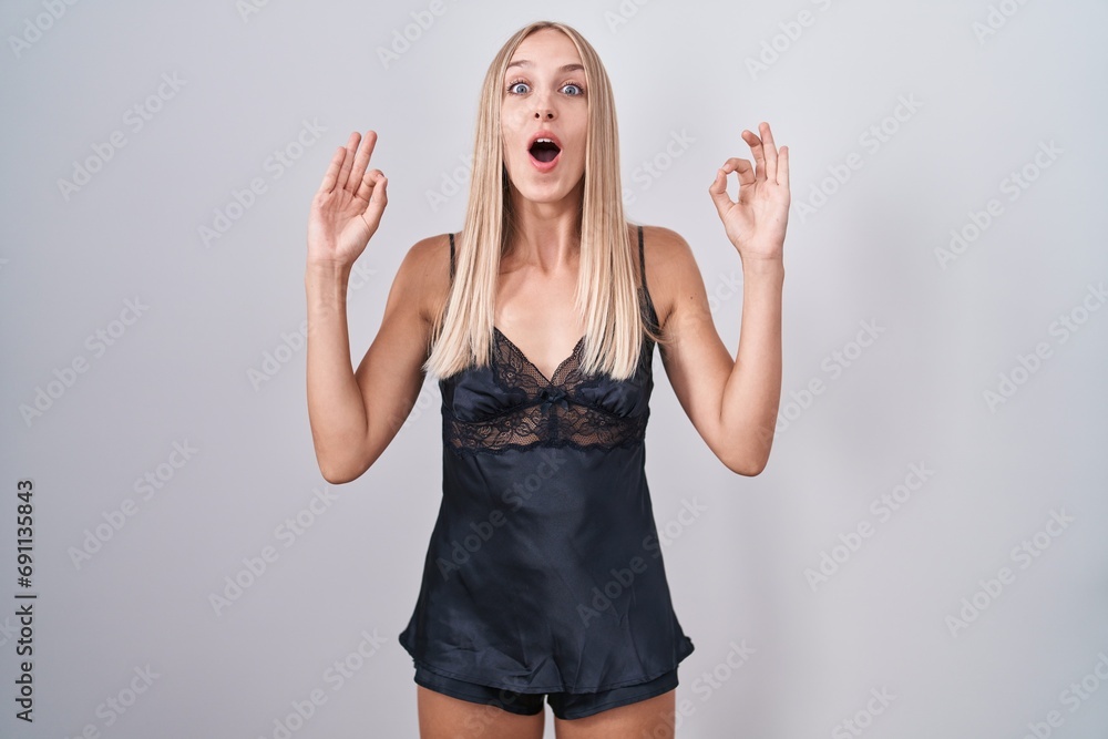 Young caucasian woman wearing nightgown looking surprised and shocked doing ok approval symbol with fingers. crazy expression Young caucasian woman wearing nightgown looking surprised and shocked doing ok approval symbol with fingers. crazy expression
