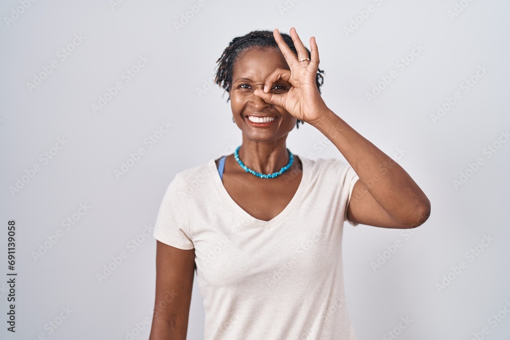 African woman with dreadlocks standing over white background doing ok gesture with hand smiling, eye looking through fingers with happy face. African woman with dreadlocks standing over white background doing ok gesture with hand smiling, eye looking through fingers with happy face.