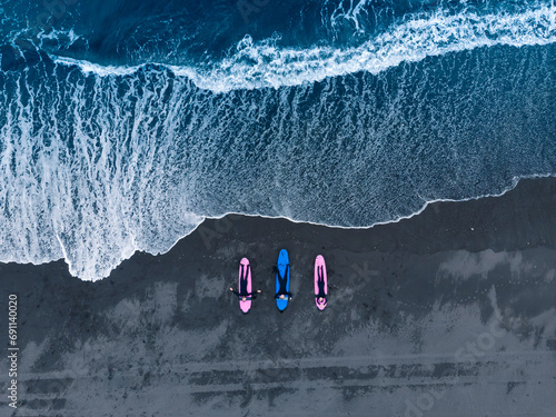 Canvas Print Aerial top view Group of friends in wetsuit going to surf at black beach