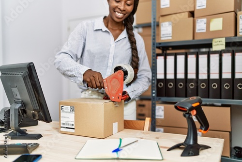African american woman ecommerce business worker packing cardboard box at office