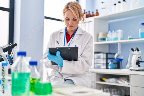 Young blonde woman scientist writing on document at laboratory