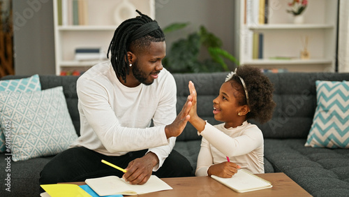 African american father and daughter smiling confident sitting on sofa drawing high five at home photo