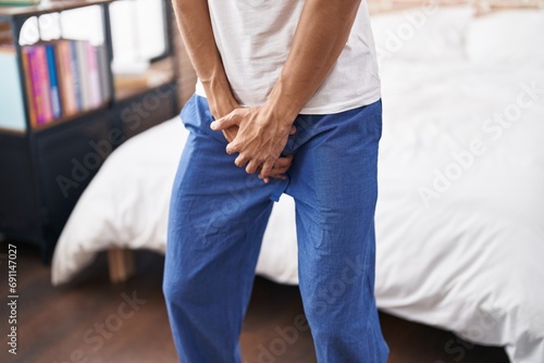 Young hispanic man covering his genitals with hands at bedroom