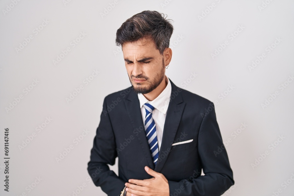 Young hispanic man with tattoos wearing business suit and tie with hand on stomach because indigestion, painful illness feeling unwell. ache concept. Young hispanic man with tattoos wearing business suit and tie with hand on stomach because indigestion, painful illness feeling unwell. ache concept.