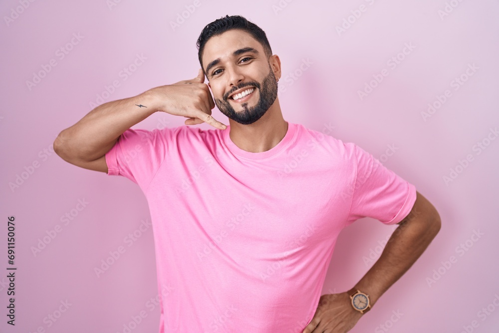 Hispanic young man standing over pink background smiling doing phone gesture with hand and fingers like talking on the telephone. communicating concepts. Hispanic young man standing over pink background smiling doing phone gesture with hand and fingers like talking on the telephone. communicating concepts.