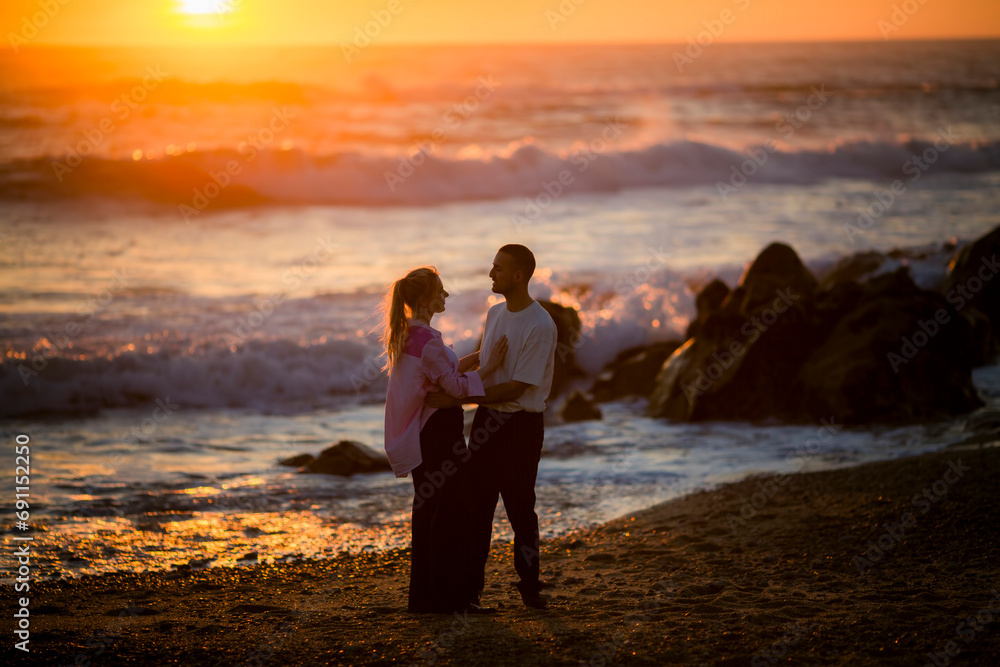 A young couple on the beach embrace during a golden sunset.