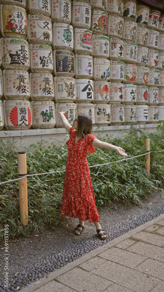 Naklejka premium Beautiful hispanic woman smiling, standing by shake barrels at meiji temple while embracing japanese culture, all while donning glasses