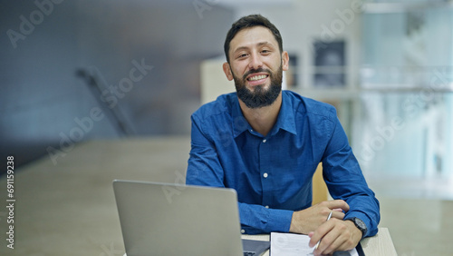 Young hispanic man business worker using laptop taking notes at the office photo
