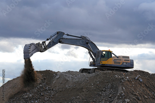 A yellow and black excavator digs up a pile of construction debris and earth on the construction of a building