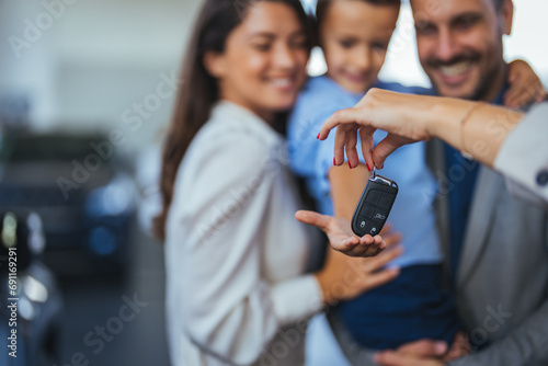 Happy parents with small kid after receiving keys for their new car in a showroom. Congratulations, we have a deal about buying a car! Happy family came to an agreement with a car salesperson