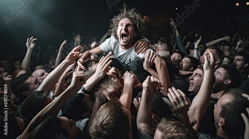 Energetic crowd surfing at a concert with an excited person being carried by a group of people in a dimly lit venue.