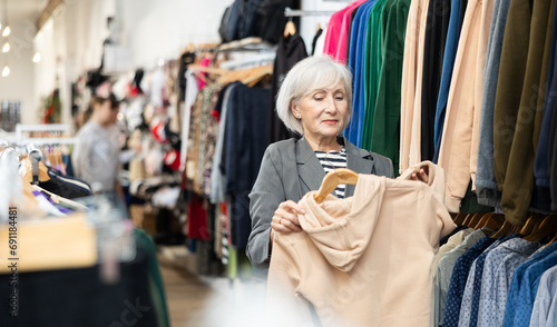 Elderly woman buyer chooses sweatshirt in clothing store.. © JackF