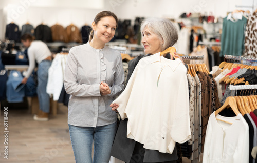 Happy middle-aged and mature women customers looking at white cardigan in large clothing store