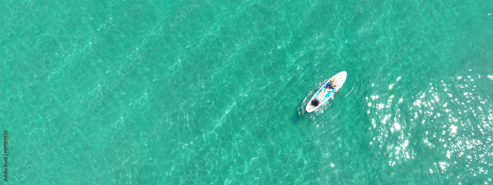 Aerial drone ultra wide panoramic photo of young unidentified woman practising paddle board or SUP in tropical Caribbean sapphire crystal clear calm waters