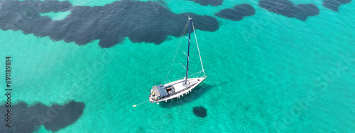 Aerial drone ultra wide panoramic photo of beautiful sail boat with white sails anchored in tropical exotic bay with emerald clear sea
