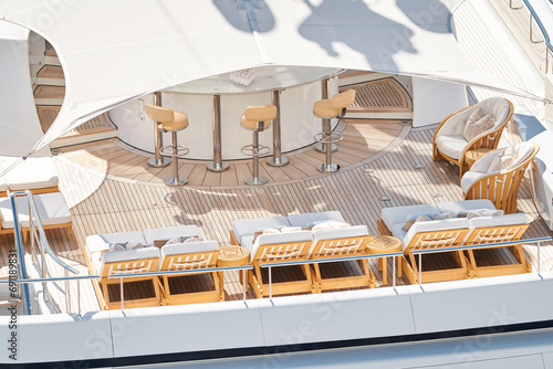 Close up footage of a relaxation area on the open teak deck of an expensive megayacht at sunny day, with awnings stretched over the deck to protect from the sun, wealth life, table and chairs