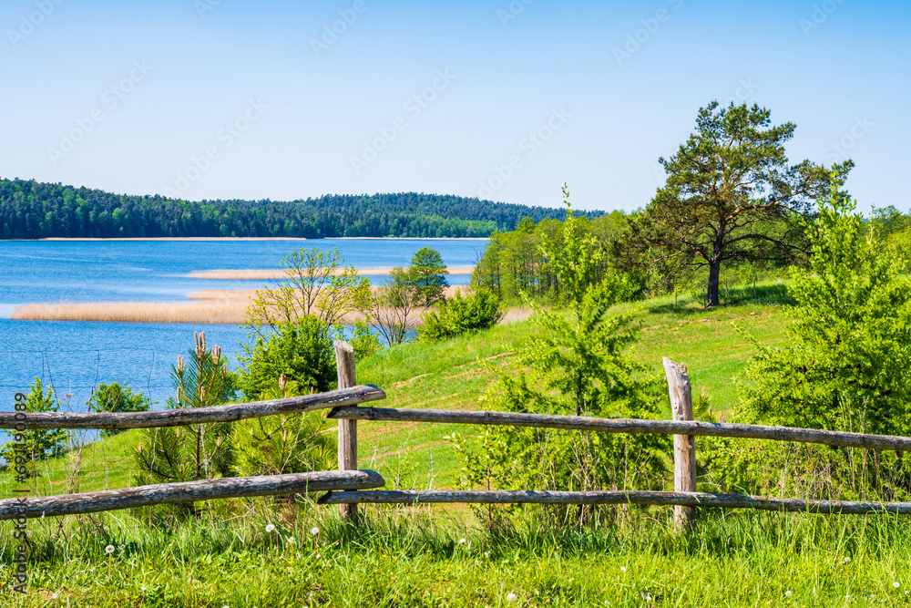 Wooden fence and wiew of green fields and Wigry lake in Wigry National Park, Podlasie, Poland