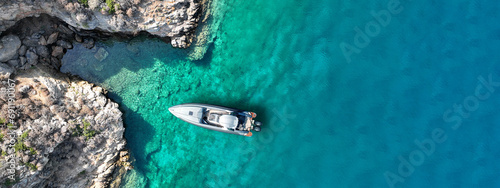 Aerial drone top down ultra wide photo with copy space of inflatable speed boat anchored in tropical exotic rocky island with emerald crystal clear sea