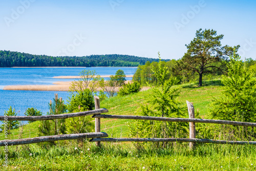 Fototapeta Naklejka Na Ścianę i Meble -  Wooden fence and wiew of green fields and Wigry lake in Wigry National Park, Podlasie, Poland