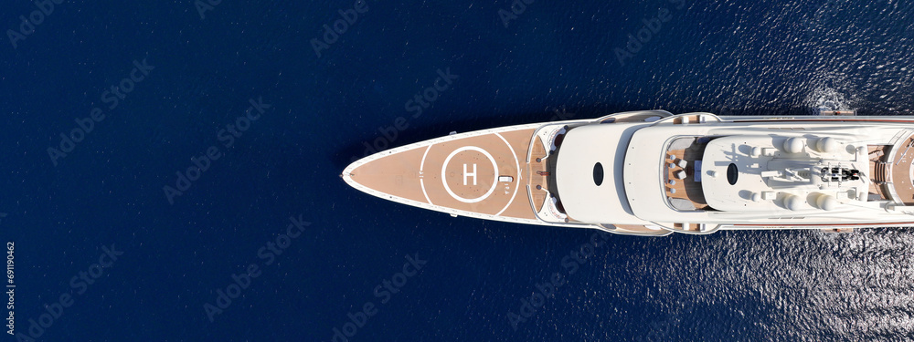 Aerial drone ultra wide panoramic photo with copy space of latest technology modern mega yacht with wooden deck and helipad anchored in deep blue Aegean sea