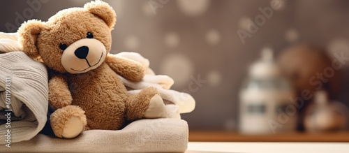 Brown stuffed teddy bear sitting on stack of clean cotton towels or clothes Childhood care clothing and plush toy for children in orphanage Doll for nursery or charity Website banner web page photo