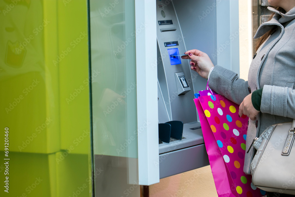 Attractive long haired brunette with shopping bags using automated teller machine. At the ATM Attractive long haired brunette with shopping bags using automated teller machine. At the ATM