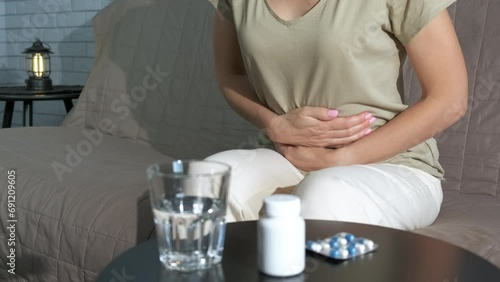 Lady with period tummy ache on sofa. A view of stressed lady sitting on sofa and suffer from pain in her belly by the table with drugs. photo