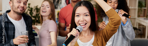 Add music to your party. Young pretty asian woman holding microphone and singing while having fun with friends at home. Playing karaoke at home.