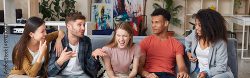 Spending nice time together. Group of young happy multicultural people in casual wear laughing while sitting together on the sofa at home. They relaxing together in the modern apartment