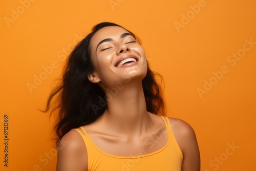 Portrait of a beautiful young asian woman laughing against orange background © Inigo