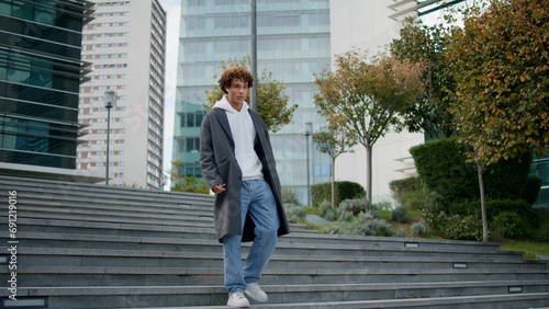 Relaxed teenager walking stairs at city street. Young man calling earphones