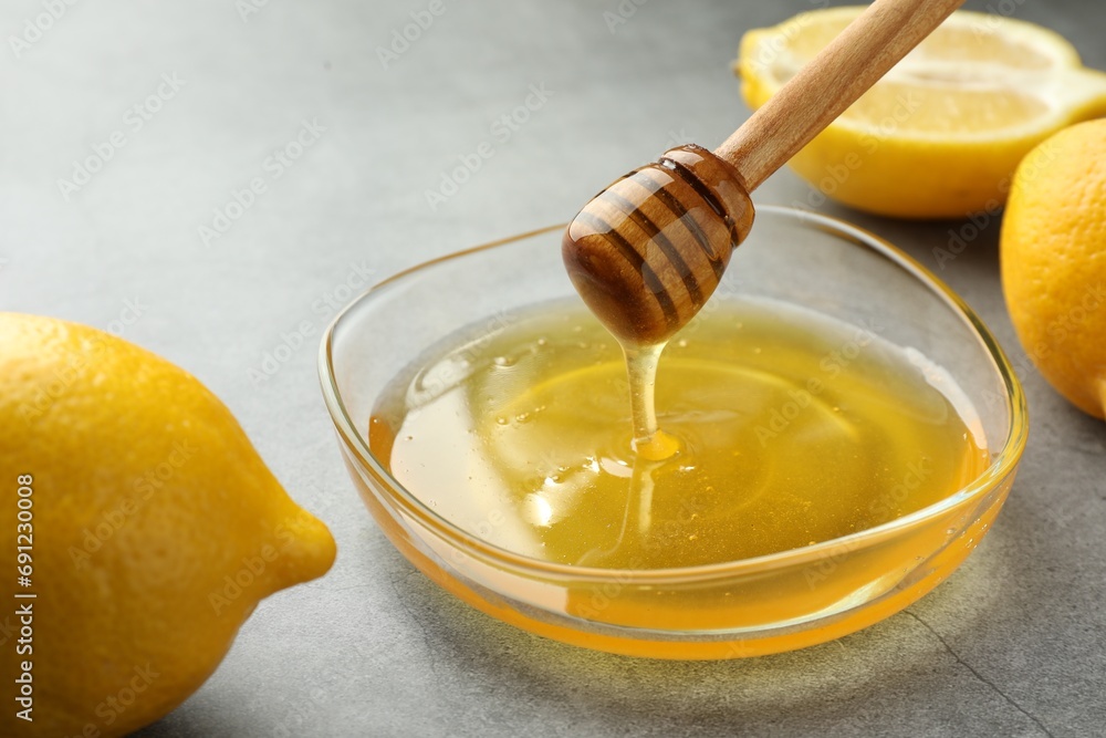 Dripping sweet honey from dipper into bowl and fresh lemons on grey table, closeup Dripping sweet honey from dipper into bowl and fresh lemons on grey table, closeup