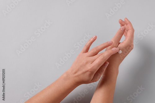 Woman applying cosmetic cream onto hand on light grey background  top view. Space for text