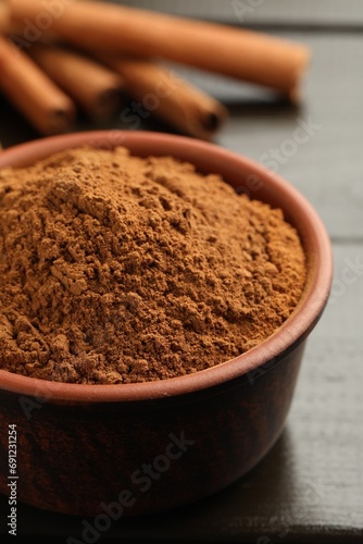 Bowl of cinnamon powder and sticks on wooden table, closeup