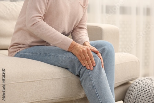 Mature woman suffering from knee pain on sofa at home, closeup. Rheumatism symptom
