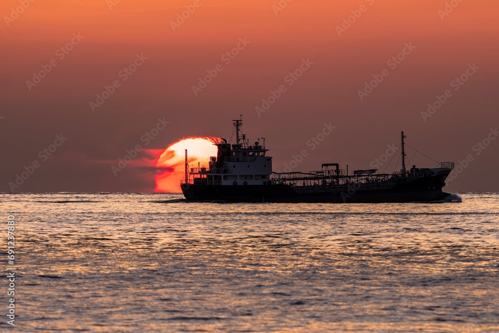 ダルマ夕日をバックに進む貨物船の情景