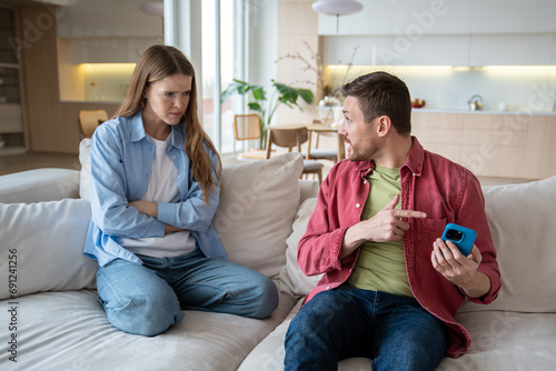 Fotografija Angry irritated woman looking at man hiding smartphone display