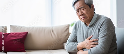 Asian senior experiencing stomach discomfort in his room. photo
