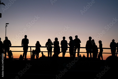 Silhouettes of people watching the skateboarders at the Venice beach skate park during sunset in California.