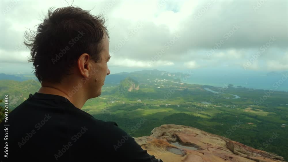 Man enjoying scenic overlook with vast green landscape and cloudy sky. Serenity and travel.