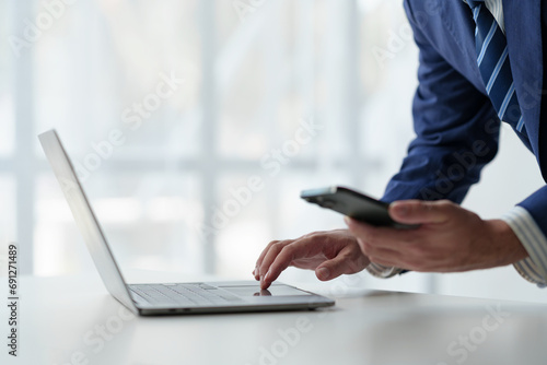 Businessman holds smartphone, checks email, checks job details on Laptop computer on white desk to point to successful business goals in office.